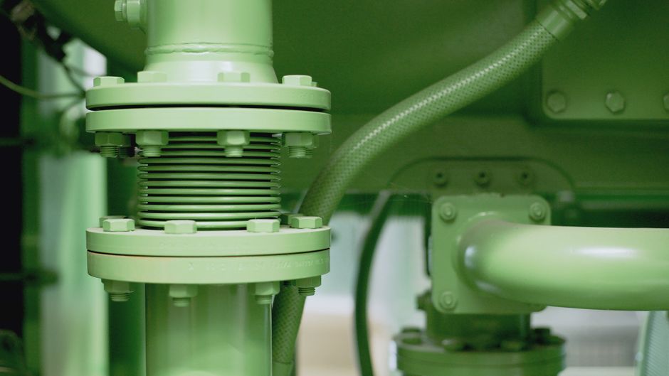 Detailed view of a green industrial pipe and valve system in a mechanical setting.